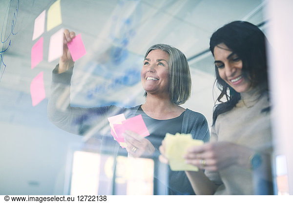 Low angle view of business professionals smiling while sticking adhesive notes on glass in office