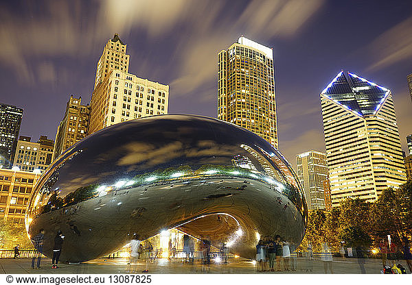 Low angle view of Cloud Gate against illuminated buildings in city