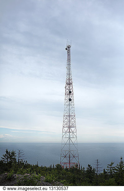 Low angle view of communication tower on field against cloudy sky
