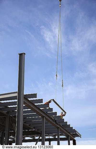 Low angle view of construction workers standing on steel girders against sky