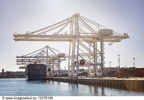 Low angle view of cranes at commercial dock against clear sky