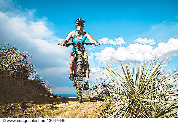 Low angle view of cyclist riding mountain bike on dirt trail against cloudy sky
