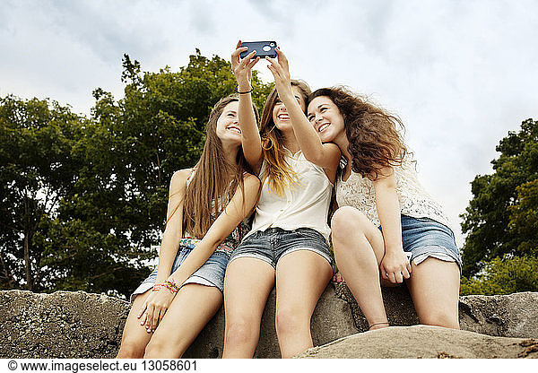 Low angle view of female friends taking selfie against sky