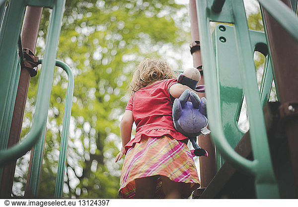 Low angle view of girl with stuffed toy standing on outdoor play equipment