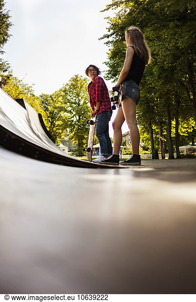 Low angle view of girls holding skateboard and standing on ramp at park