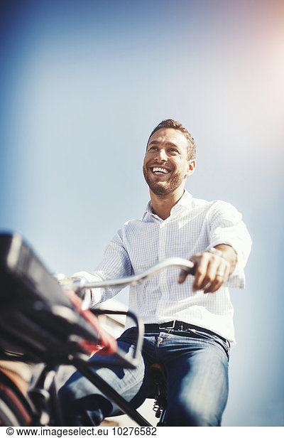 Low angle view of happy businessman riding bicycle against blue sky