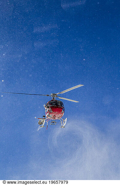Low angle view of helicopter in flight blowing swirling snow
