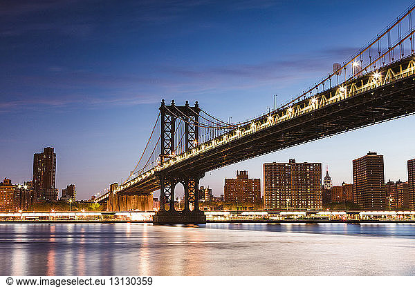 Low angle view of illuminated Manhattan Bridge over East river against blue sky at dusk