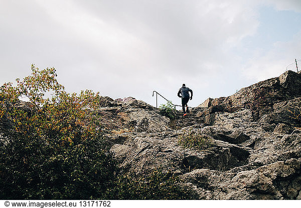 Low angle view of male athlete climbing rocks on hill against sky