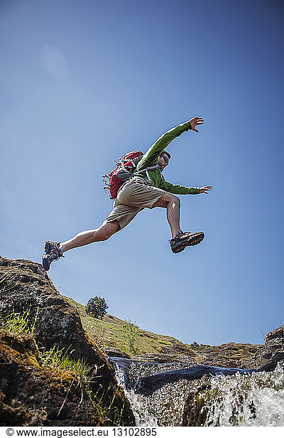 Low angle view of male hiker jumping over stream