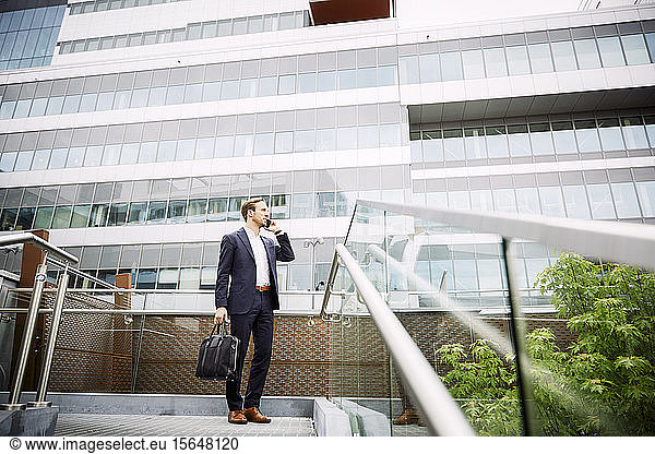 Low angle view of male lawyer talking on smart phone while standing against building
