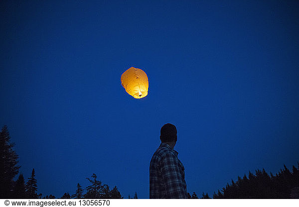 Low angle view of man and illuminated paper lantern against blue sky