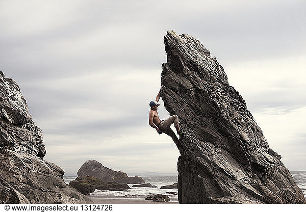 Low angle view of man climbing rock formation against cloudy sky