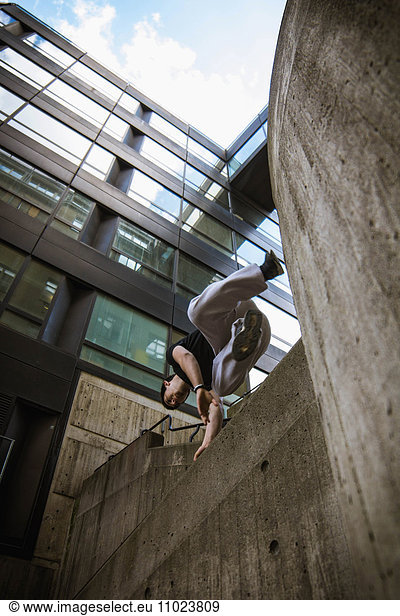 Low angle view of man jumping over retaining wall by modern building