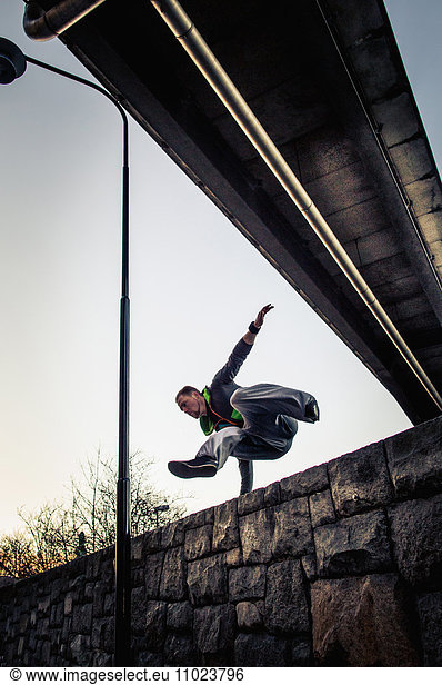 Low angle view of man jumping over surrounding wall under bridge