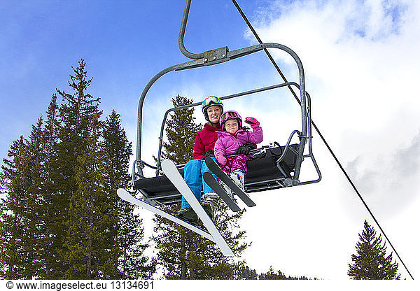 Low angle view of mother and daughter sitting in ski lift against sky