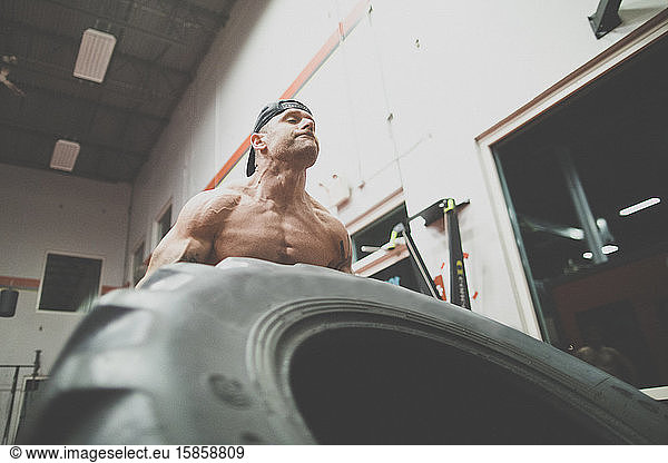 low angle view of muscular man lifts large tire at the gym