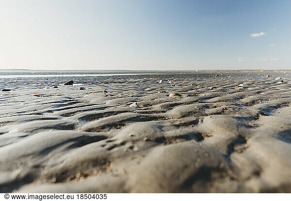 Low angle view of ripples in sand at low tide on beach with blue sky