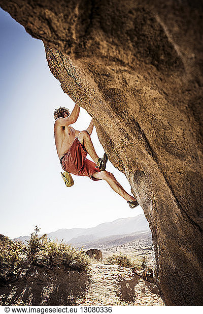 Low angle view of shirtless hiker climbing rock against clear sky Low ...