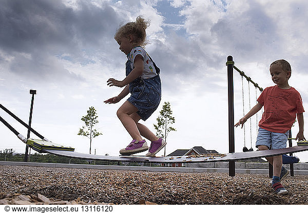 Low angle view of siblings playing on outdoor play equipment at playground against storm clouds