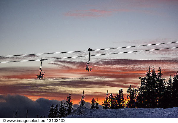 Low angle view of ski lift against cloudy sky during sunset