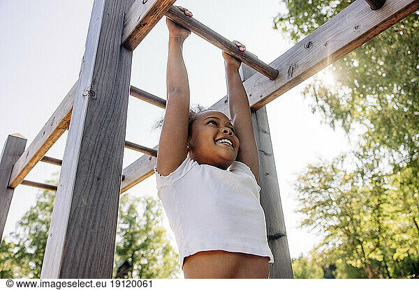Low angle view of smiling girl hanging while doing monkey bars at summer camp