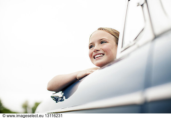 Low angle view of smiling girl travelling in car against clear sky