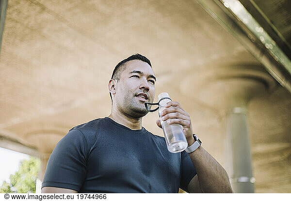 Low angle view of tired man drinking water from bottle during workout