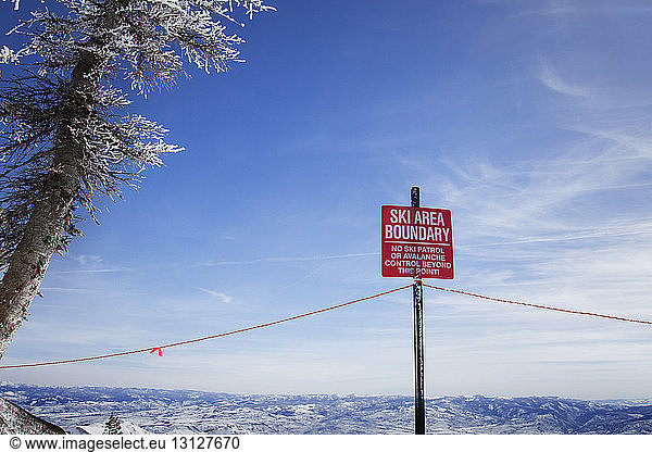 Low angle view of warning sign against sky during winter