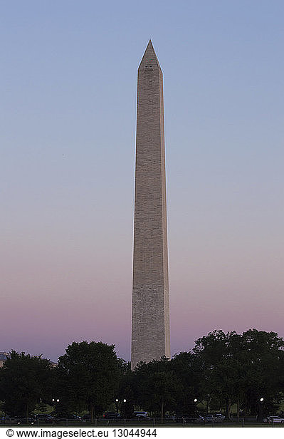 Low angle view of Washington Monument amidst trees against clear sky during sunset