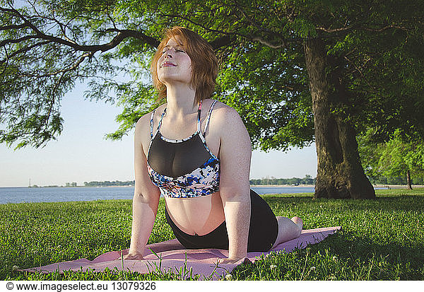 Low angle view of woman doing cobra pose on exercise mat at park