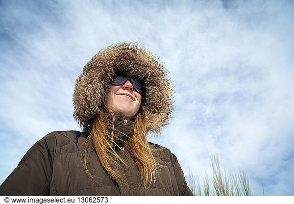 Low angle view of woman wearing fur hood against cloudy sky
