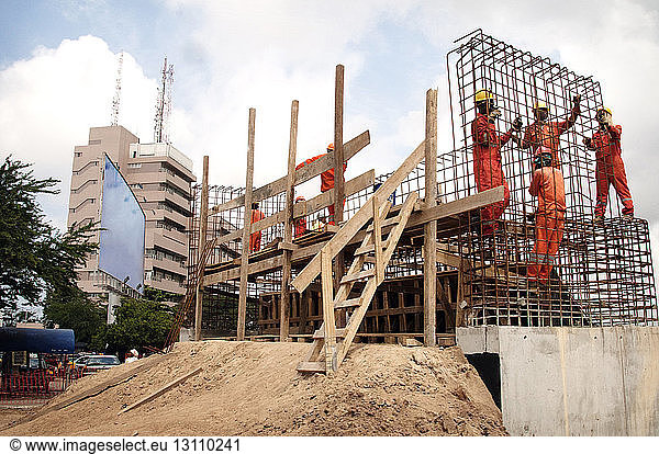 Low angle view of workers working at construction site against cloudy sky