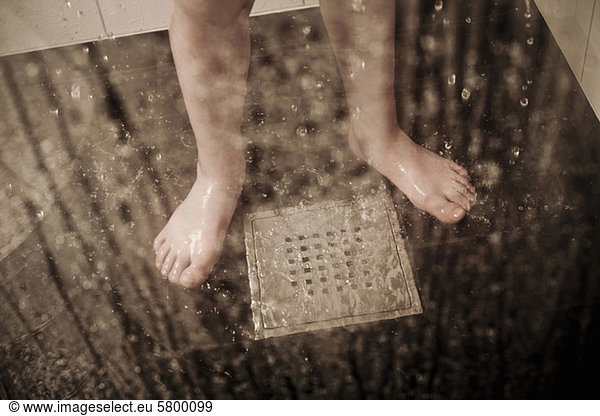 Low section of a boy standing by drain in domestic bathroom