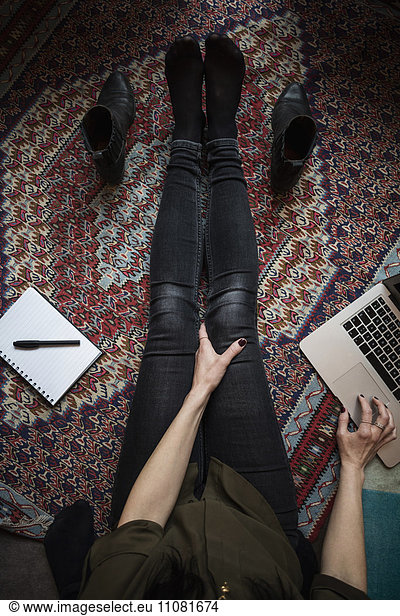 Low section of blogger using laptop while sitting on carpet