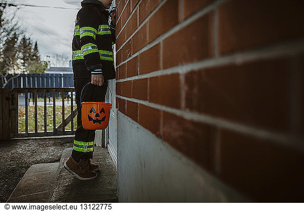Low section of boy holding Halloween bucket while standing by door