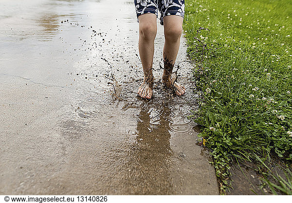Low section of boy jumping in dirty puddle