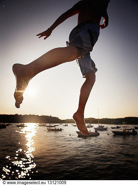 Low section of boy jumping in sea during sunset