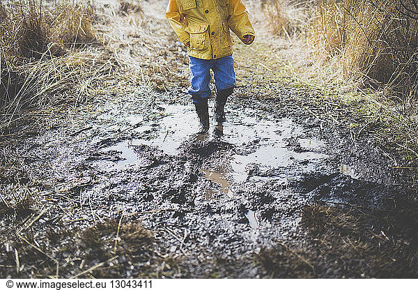 Low section of boy walking in dirty puddle