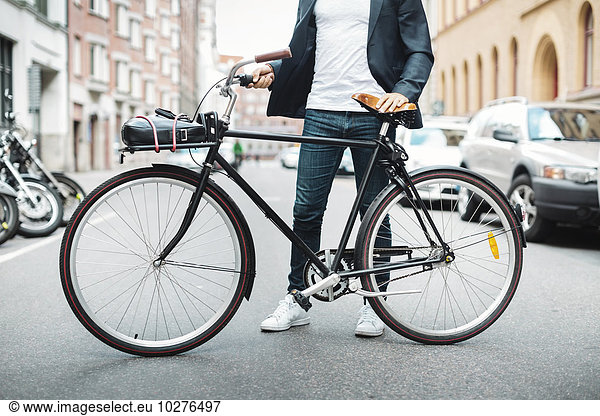 Low section of businessman with bicycle standing on city street