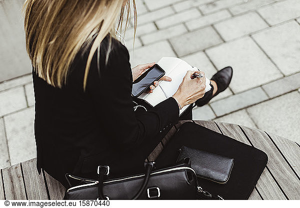 Low section of businesswoman writing while sitting outdoors