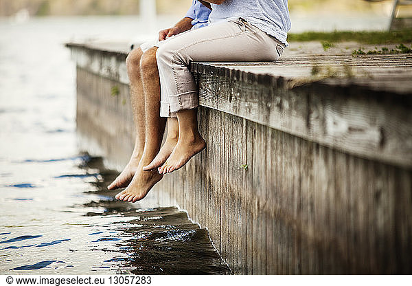 Low section of couple sitting on pier in lake