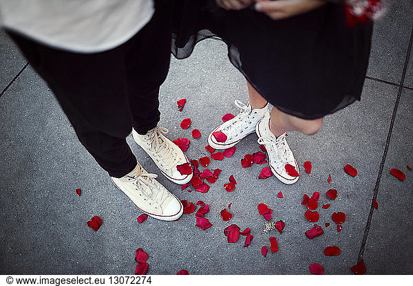 Low section of couple standing on footpath with red rose petals