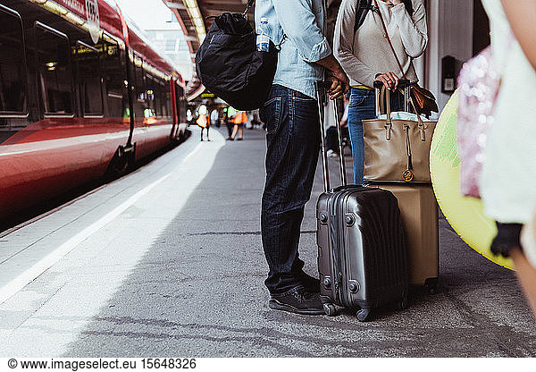 Low section of couple with luggage standing on railroad station platform