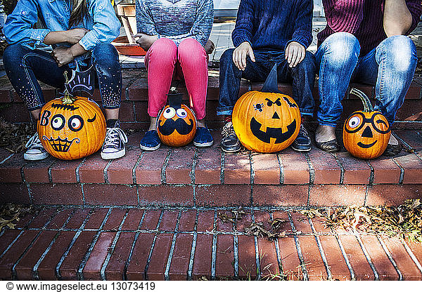 Low section of family sitting with decorated pumpkins on steps during Halloween