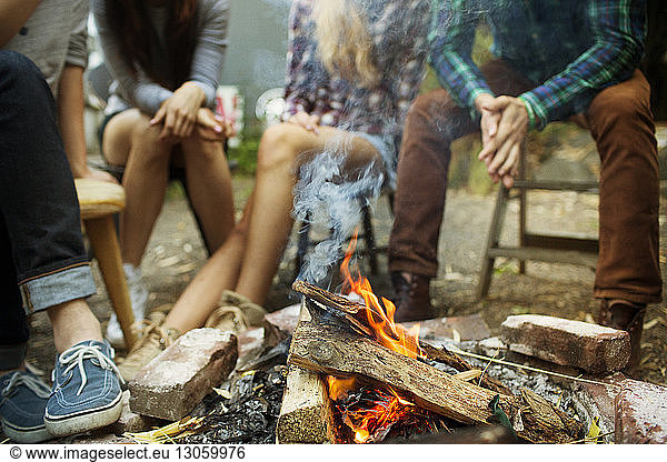 Low section of friends sitting by bonfire