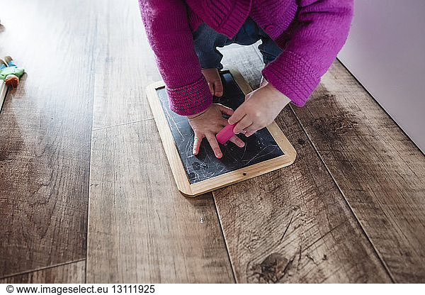 Low section of girl crouching with slate and eraser on hardwood floor