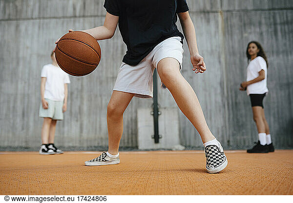 Low section of girl dribbling basketball while playing in court