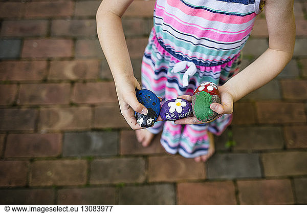 Low section of girl holding painted stones while standing on footpath