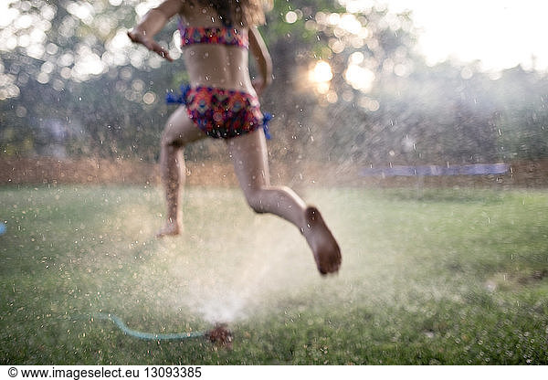 Low section of girl in swimwear running on grassy field at yard